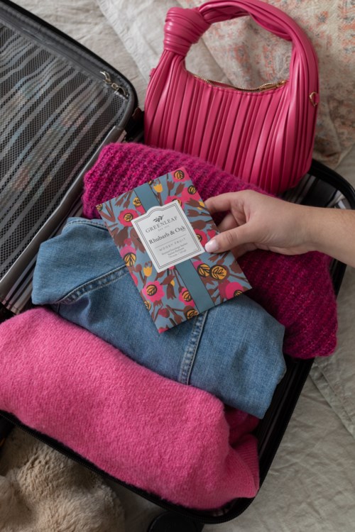 Salkku sisältää vaatteita, pinkin laukun ja kirjan värikkäällä kannella. Vaatteisiin kuuluu pinkkejä ja sinisiä kankaita.