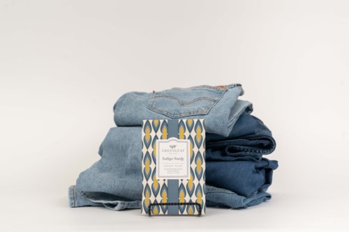 En hög av vikta blå jeans med en dekorativ etikett framför, mot en enfärgad vit bakgrund.
