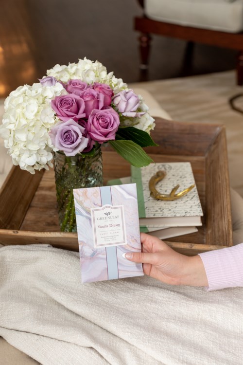 Een hand houdt een kaart voor een boeket rozen en witte bloemen op een houten tafel.