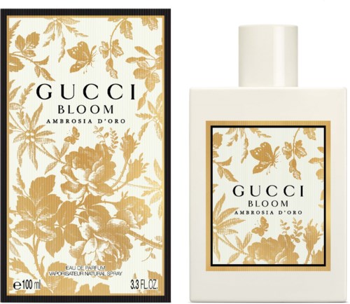 En parfymflaske og æske med guldblomsterdesign og sorte rammer. Flasken er hvid med et matchende label.