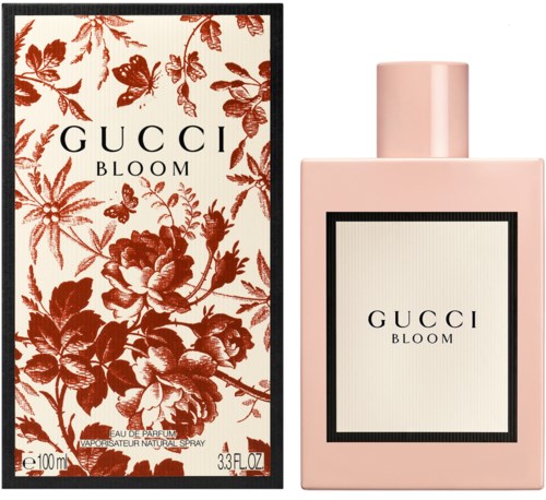 Różowa butelka perfum z jasnym etykietą i czarną ramką, obok ozdobne pudełko z czerwonymi kwiatami i czarną ramką.