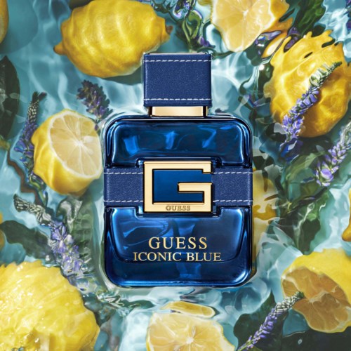 En blå parfymflaske mærket Guess Iconic Blue, omgivet af citroner og lavendel blomster på vand.