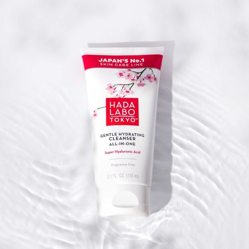 A white tube of Hada Labo Tokyo gentle hydrating cleanser with pink cherry blossom design, on a white textured background.