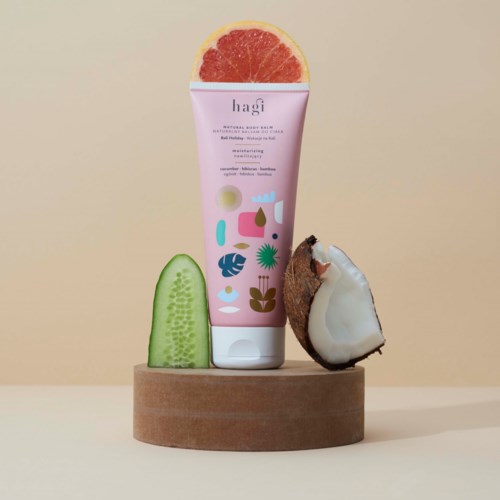 En rosa tube merket 'hagi', en skivet agurk, en kokosnøtt og halve grapefrukt på en trebunn.