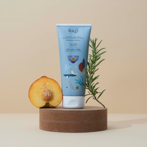 A blue tube of skincare cream with a plant and a peach on a wooden platform.