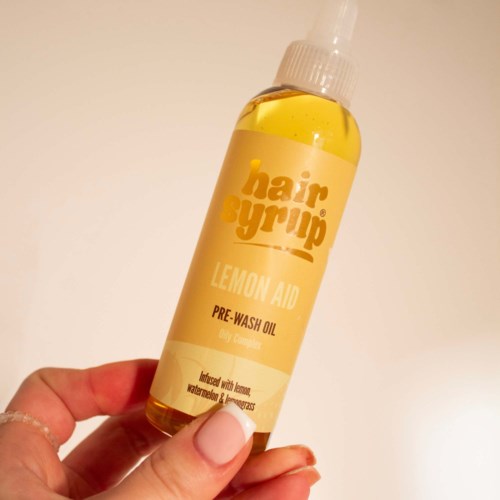 En liten gul flaska med spraylock märkt 'hair syrup' med förtvättsolja med citron doft.