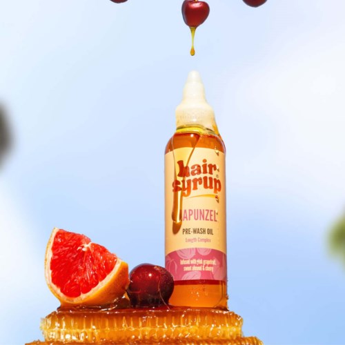 En flaska hårsirup omgiven av grapefrukt, körsbär, honungskaka och droppar som faller från ovan.