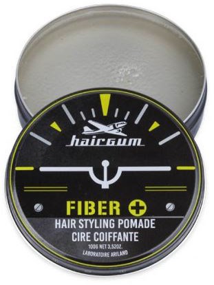 En rund beholder med hårstylingpomade, svart etikett, gul og hvit tekst, og en logo av en fugl eller ørn.