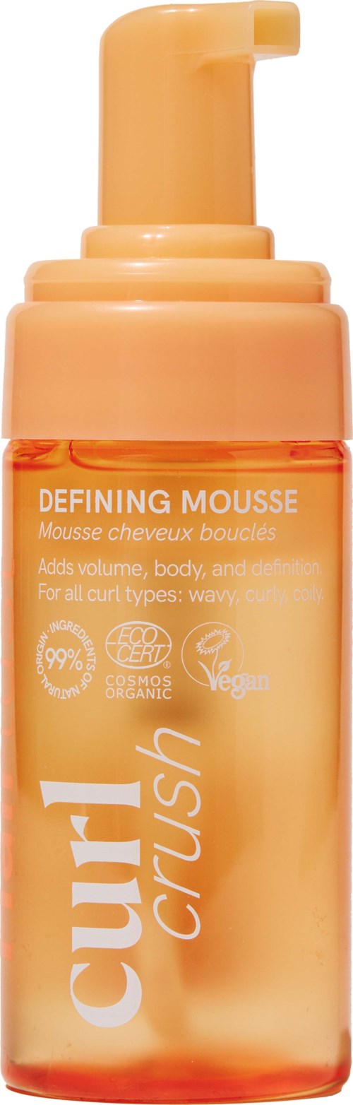 Een perzikkleurige fles met pomp voor definërende mousse, label curl crush, voor volume en definitie bij golvend haar.