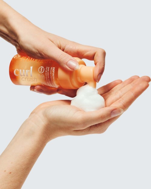 Oranje shampoo fles die schuim in iemands hand schenkt.