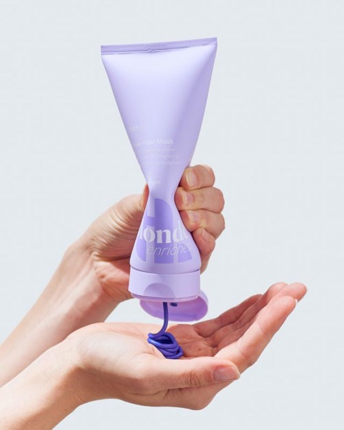 Een hand houdt een lavendelkleurige tube haarmasker met wat product eruit gedrukt.