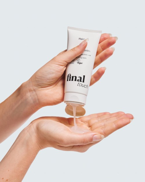 Handen die uit een witte tube haar gel op de handpalm knijpen.