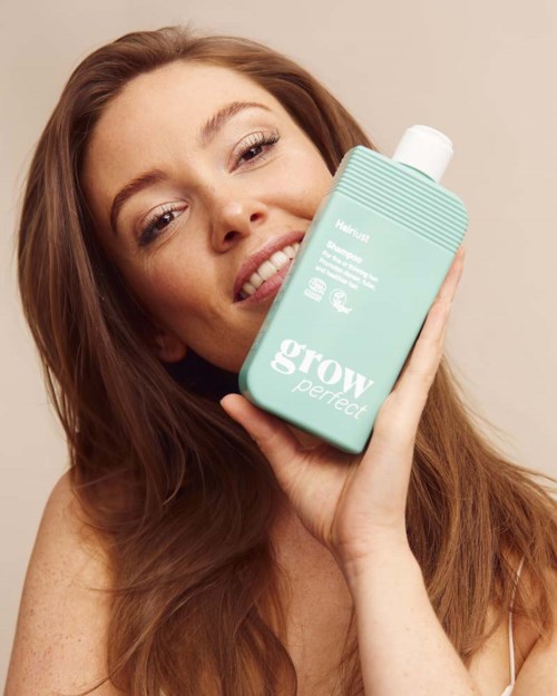 Een lachende vrouw met lang golvend haar houdt een turquoise fles met grow perfect huidverzorging.