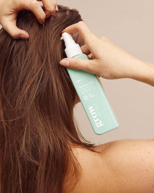 Persoon die haarproduct sprayt op haar, close-up van bruin haar en een lichtblauwe sprayfles.