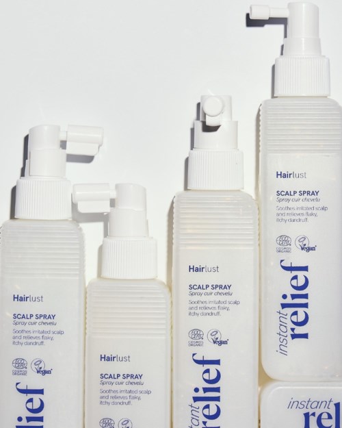 Vier witte flessen Hairlust hoofdhuid spray met spraykoppen, gemarkeerd als verzachtend en kalmerend.