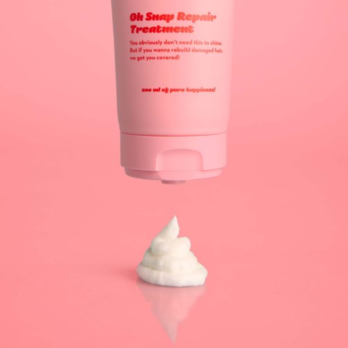 A pink bottle of hair treatment with a dollop of white cream underneath against a pink background.
