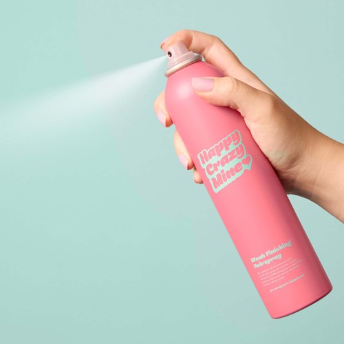 Eine Hand sprüht eine pinke Dose mit der Aufschrift 'Happy Crazy Mine' gegen einen hellblauen Hintergrund.