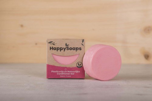En rosa cirkulär tvål bredvid en kartonglåda märkt 'Happy Soaps' på en träyta.