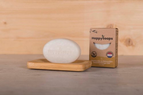 En tvål och dess förpackning på ett träfat, märkt 'HappySoaps,' med en ljus träbakgrund.