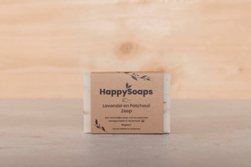 En sæbe med mærket "HappySoaps" er placeret på en lys træoverflade. Sæben har beroligende lavendel- og patchouli duft.