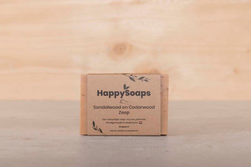 En lille sæbeæske mærket 'Happy Soaps' med ingredienser sandalwood og cedarwood, på en træoverflade.