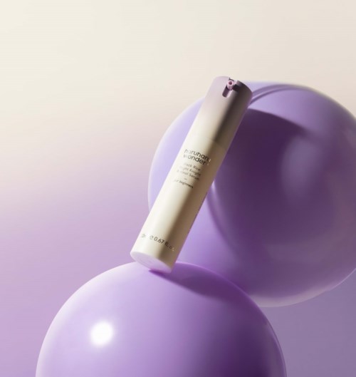 Een witte cilindervormige fles op twee paarse ballonnen, met een lichtpaarse achtergrond.