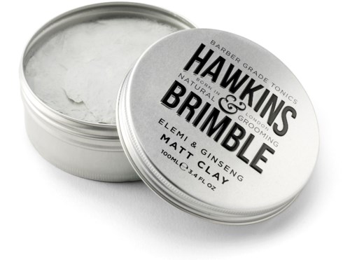 En rund öppen burk innehåller vit hårvax, märkta Hawkins & Grimble med naturliga ingredienser.