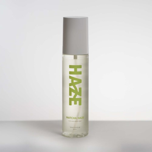 En gennemsigtig sprayflaske med gråt låg og grøn tekst HAZE på en lys baggrund.