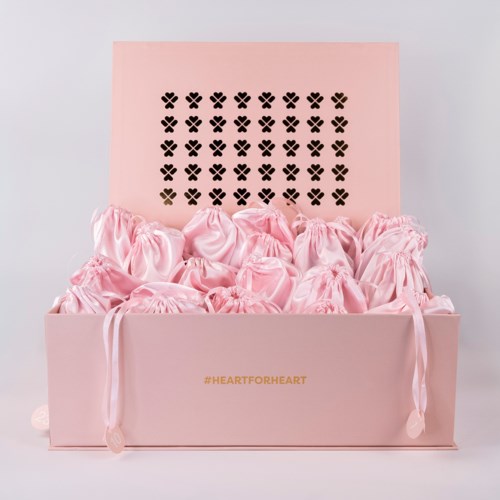 Rosa låda fylld med små rosa påsar, lock med svarta hjärtformade mönster och hashtag #HEARTFORHEART.
