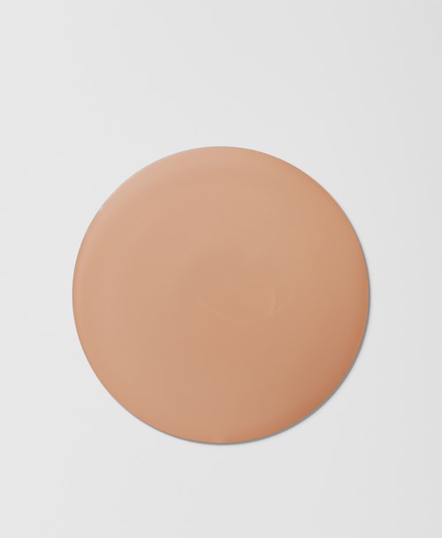 En rund, beige sminksvamp med flat overflate på en grå bakgrunn.