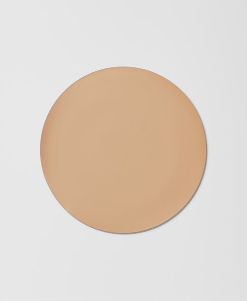 En rund beige sminke-kompakt med et enkelt, glatt deksel på en hvit overflate.