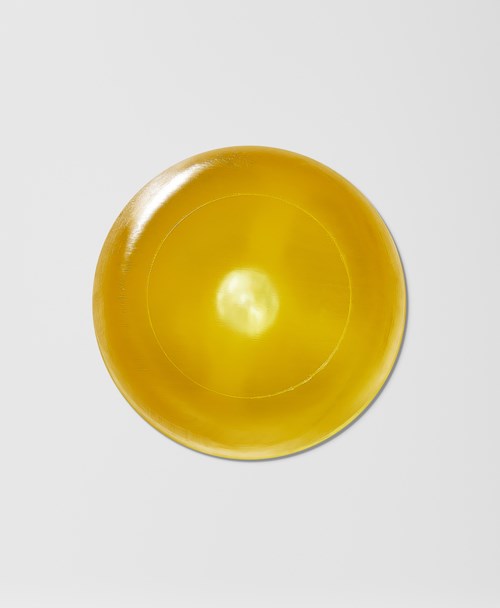 En rund, skinnende, gul gjenstand som minner om en sitron eller en ball på en vanlig hvit overflate.