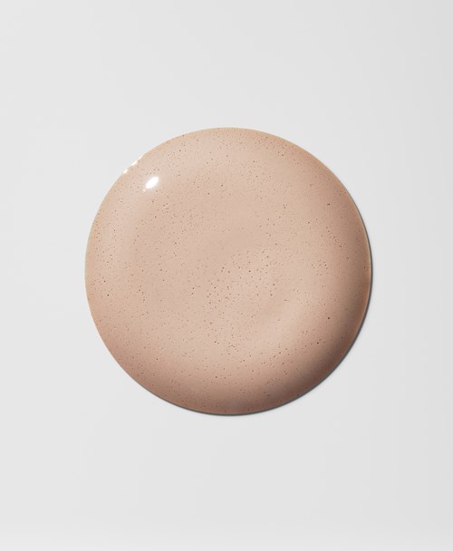 Ett beige, prickigt kosmetiskt produkt eller kräm i en rund behållare på en ren, vit bakgrund.