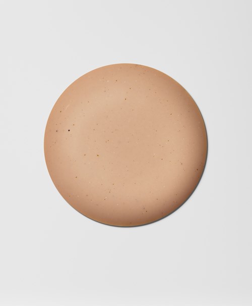 Een ronde, beige voorwerp met kleine donkere vlekken op een lichtgrijze achtergrond.