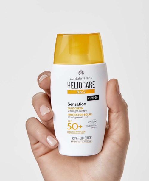 Hand som håller i en vit och gul solkrämflaska med solskydd SPF 50+ och etikettuppgifter.