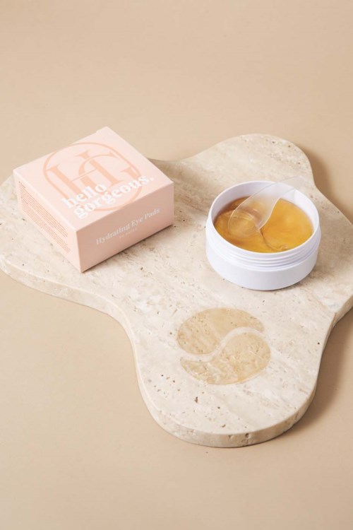 En rund hvid beholder med gel eller creme, en pink æske og en stenoverflade med en logo. Opsætningen er enkel og ren.