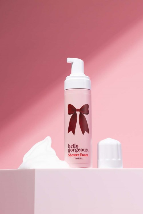 Shower foam bottle with a bow label and a dollop of foam on pink background.