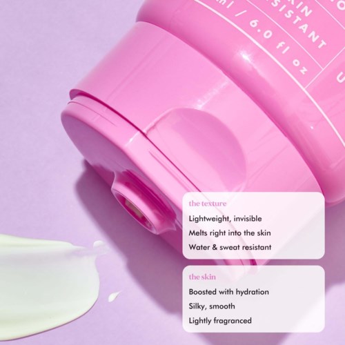A pink bottle lies on a light purple surface, with text describing its features: lightweight, melting into skin, water-resistant, hydrating, silky, lightly scented.