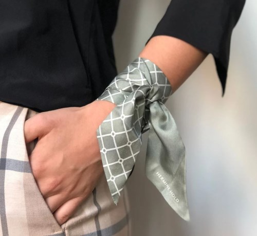 En hand med en mönstrad scarf knuten runt handleden, som bär en svart ärm och beige kläder.