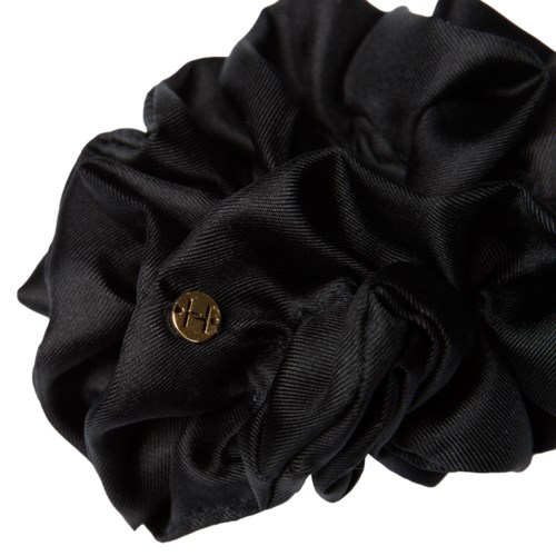 En svart tygscrunchie med en liten guldlogo eller charm fastsatt.