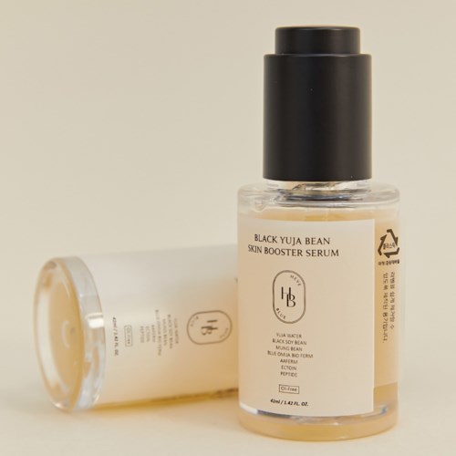 En liten genomskinlig flaska med svart lock, märkt Black Yuja Bean Skin Booster Serum, ligger bredvid en liknande flaska.