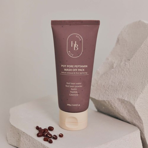 En lila tub märkt 'Pot Pore Peptamin Wash Off Pack' med ingredienser listade, står på en vit yta med små röda bönor.