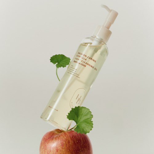 En klar flaska med pump står på ett äpple med gröna blad, mot en enkel bakgrund.