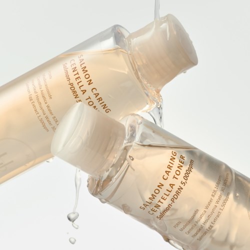 Två hudvårdsflaskor märka Salmon Caring Centella Toner är staplade och droppar med vätska.