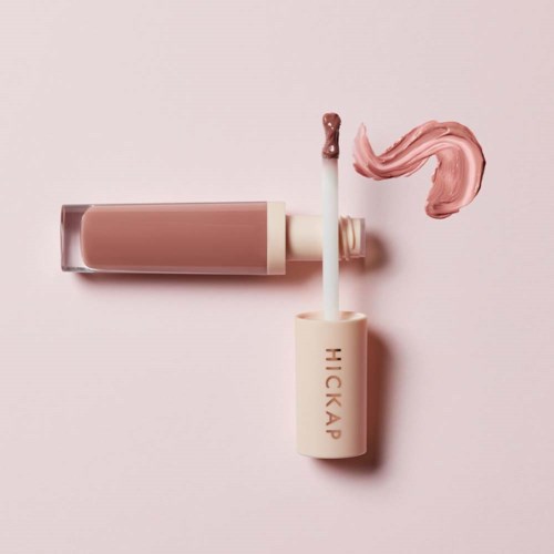 Leppeglansrør og pensel med rosa gloss på en pastell rosa bakgrunn.