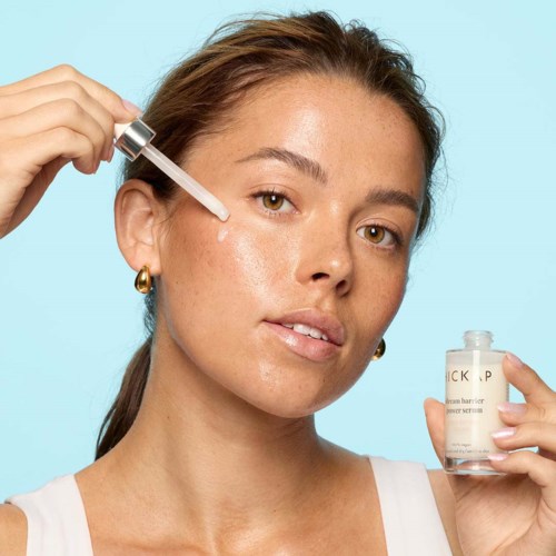Eine Frau trägt Serum mit einer Pipette auf ihr Gesicht auf, hält eine kleine Flasche Hautpflegeprodukt.