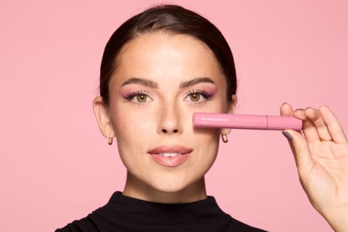 Eine Frau mit Pink-Make-up hält einen pinken Gegenstand an die Nase vor einem rosa Hintergrund.