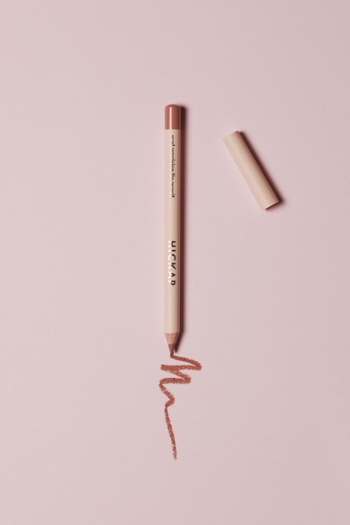 En rosa leppestift med lokket ved siden av, som tegner en bølgende linje på rosa bakgrunn.