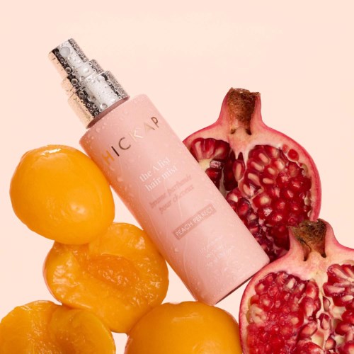 En rosa sprayflaska märkt 'peach nectar' med granatäppelklyftor och persikor runt den.