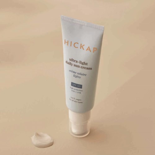 En vit tub med solkräm med märket 'HICKAP' och SPF 50, med kräm bredvid.